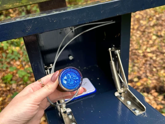 Stempel-Nordsee-Reisepass-Torfspitt-Kayhausen-Bad-Zwischenahn.jpg Hand hält blauen Nordsee-Reisepass-Stempel vom Torfspitt Kayhausen vor geöffneter Stempelbox.