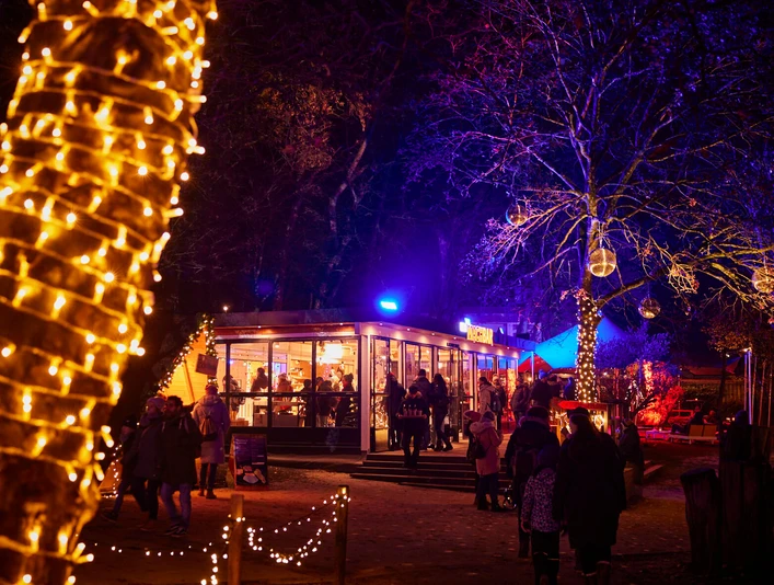 Blackfoot Winterland Ein festlich beleuchteter Wintermarkt in der Dämmerung, Besucher schlendern entlang bunter Lichter.A festively illuminated winter market at dusk, visitors stroll along colorful lights.