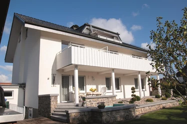 Haus Waltraut Menne - Außenansicht Zweistöckiges helles Wohnhaus mit Balkon, Steinsockel, Terrasse und gepflegtem Vorgarten.
