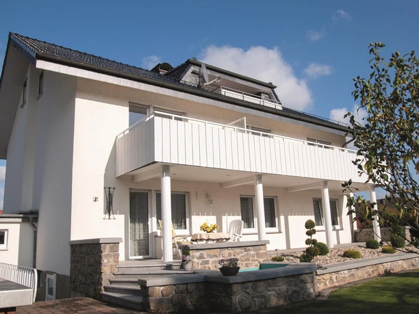 Haus Waltraut Menne - Außenansicht Zweistöckiges helles Wohnhaus mit Balkon, Steinsockel, Terrasse und gepflegtem Vorgarten.
