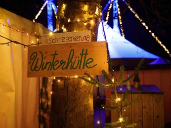 Blackfoot Winterland Ein rustikales Schild mit der Aufschrift "Winterhütte" leuchtet festlich im Lichterglanz.A rustic sign with the inscription "Winterhütte" (winter hut) shines festively in the glow of the lights.