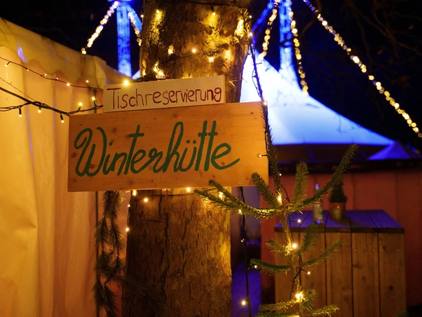 Blackfoot Winterland Ein rustikales Schild mit der Aufschrift "Winterhütte" leuchtet festlich im Lichterglanz.