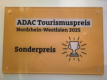 Plakette ADAC Tourismuspreis 2025.jpg ADAC Tourismuspreis Nordrhein-Westfalen 2025 Sonderpreis mit Pokal-Symbol auf gelbem Schild.ADAC Tourism Award North Rhine-Westphalia 2025 Special prize with trophy symbol on yellow sign.
