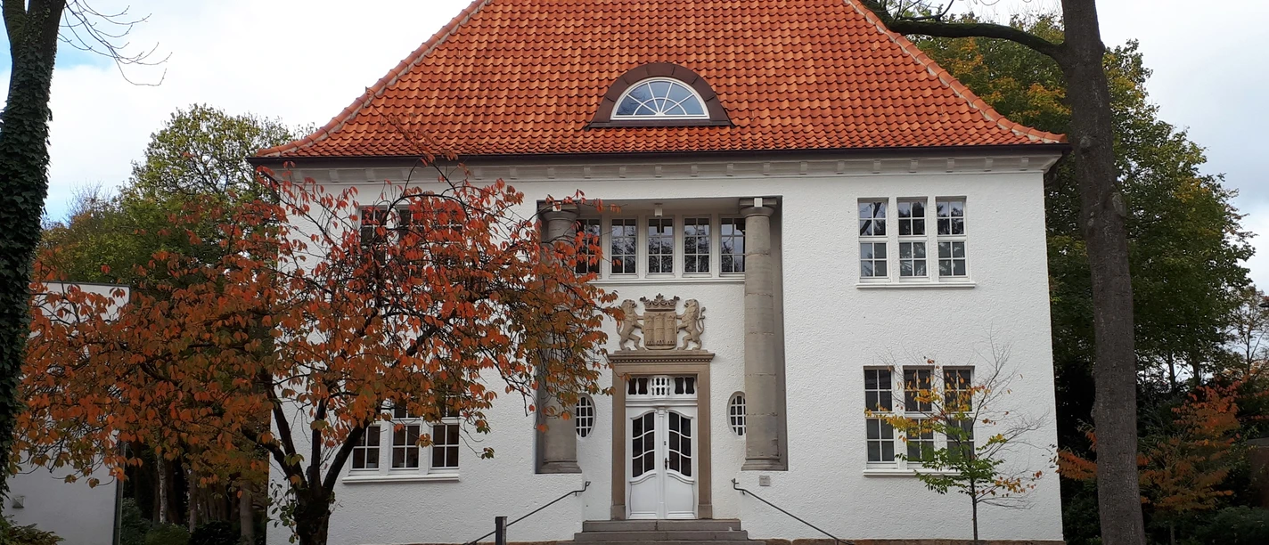 Kunst- und Kulturvilla 100 Jahre nach Fertigstellung.jpg Weißes zweigeschossiges Haus mit rotem Ziegeldach, Säulenportal und herbstlich gefärbten Bäumen.
