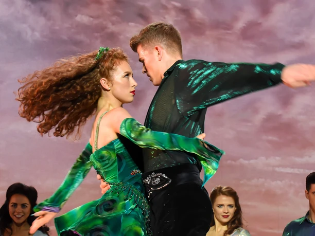 Riverdance 30 – The New Generation A powerful dance moment: a couple in bright green, expressive in front of a dramatic backdrop.