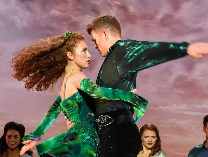 Riverdance 30 – The New Generation Ein kraftvoller Tanzmoment: Ein Paar in leuchtendem Grün, ausdrucksstark vor einer dramatischen Kulisse.A powerful dance moment: a couple in bright green, expressive in front of a dramatic backdrop.