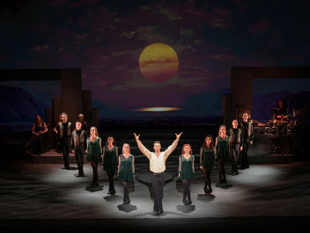 Riverdance 30 – The New Generation Dancers on a stage, sunset with a magical atmosphere in the background.