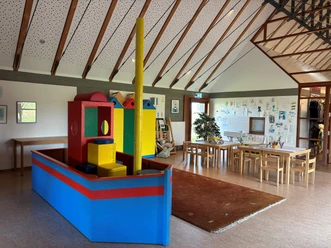 Kinderspielzimmer Wremen Helles Spielzimmer mit buntem Holzschiff, Maltischen und Kindersitzecke unter hohem Dach.