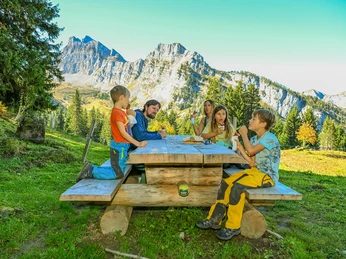 Brätelstelle GrimmiJutz beim Posten 4 Eine Familie sitzt an einem Holztisch und isstA family sits at a wooden table and eatsUne famille est assise à une table en bois et mange