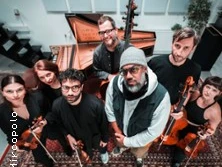 Eine Musikgruppe steht in einem Studio mit Instrumenten wie Geige und Kontrabass.