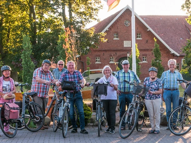 Radfahrer©R. Heskamp.jpg Gruppe älterer Radfahrer steht lachend mit Fahrrädern vor einem roten Backsteinhaus in Lingen.