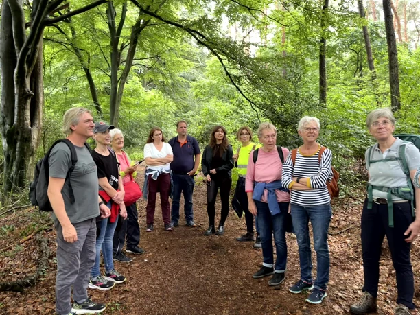 Wanderung Gruppe von Wandernden steht auf einem Waldweg, umgeben von dichten grünen Bäumen.