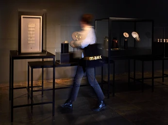 Ausstellung: 'Von Louise Bourgeois bis Yoko Ono. Schmuck von Künstlerinnen' Eine Person im Museum in Bewegung, umgeben von Kunstwerken in einem gedämpft beleuchteten Ausstellungsraum.A person in motion in a museum, surrounded by works of art in a dimly lit exhibition space.