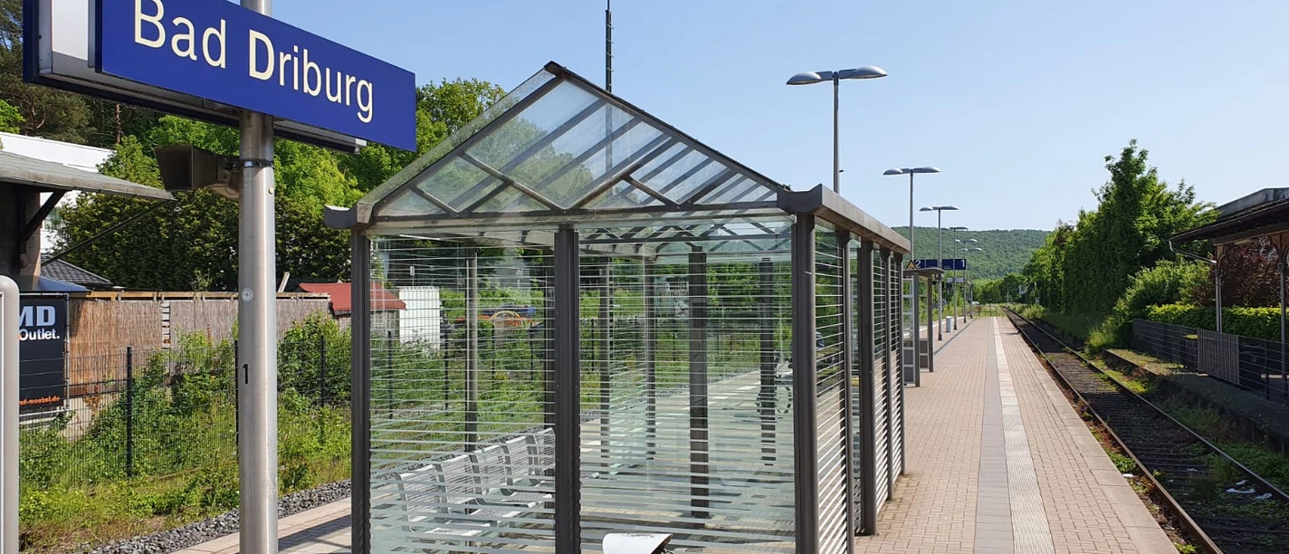 Bad-Driburg-Bahnhof Gleisanlage am Bahnhof Bad Driburg mit überdachtem Wartebereich und Blick auf grüne Hügel.