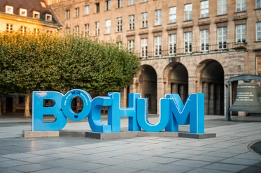 Große blaue Buchstaben formen das Wort "BOCHUM" vor historischen Arkaden.