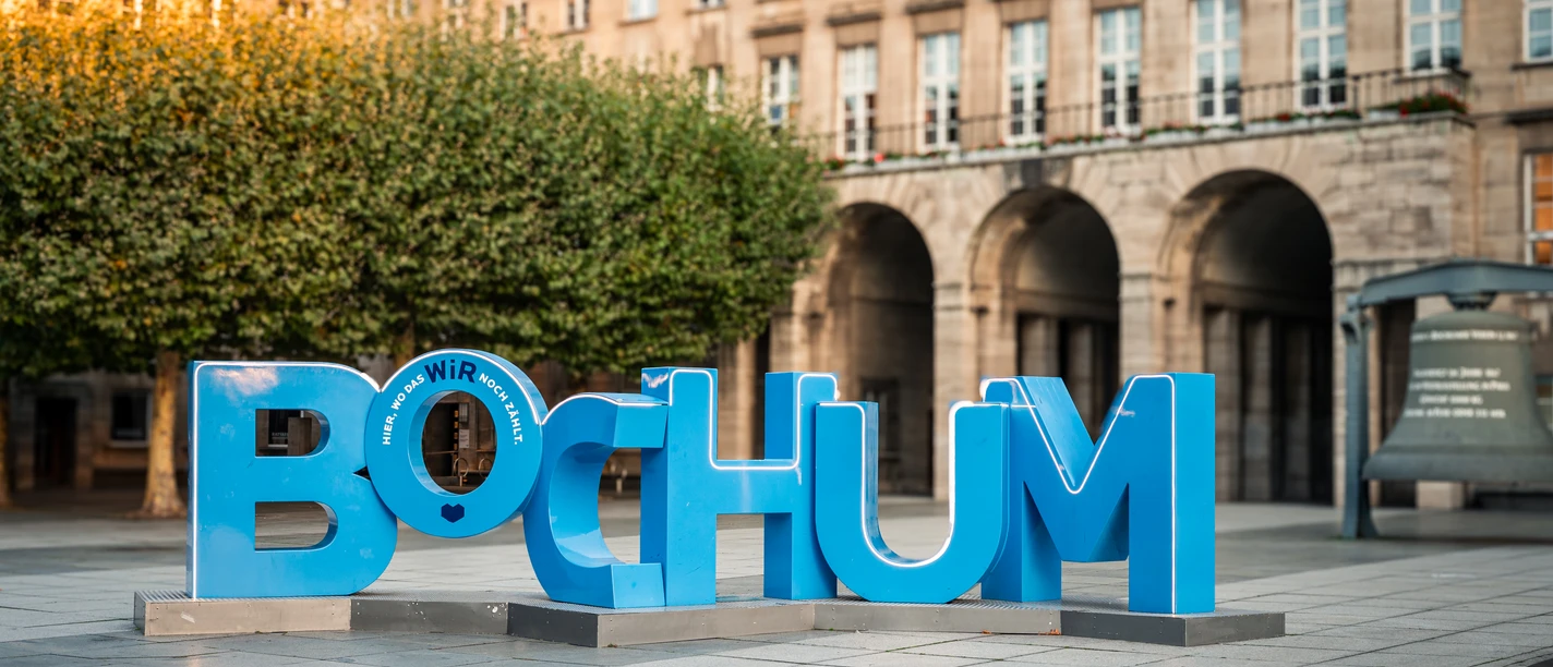 Große blaue Buchstaben formen das Wort "BOCHUM" vor historischen Arkaden.