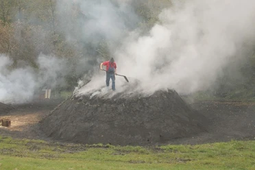 Der Köhler Reinhold Wagner kontrolliert die Rauchöffnung am Meiler. So stellt er sicher, dass das Holz bei ca. 300 °C verkohlt und nicht höhere Temperaturen eintreten, bei denen das Holz verbrennen würde.