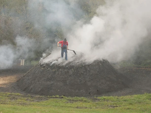 Der Köhler Reinhold Wagner kontrolliert die Rauchöffnung am Meiler. So stellt er sicher, dass das Holz bei ca. 300 °C verkohlt und nicht höhere Temperaturen eintreten, bei denen das Holz verbrennen würde.