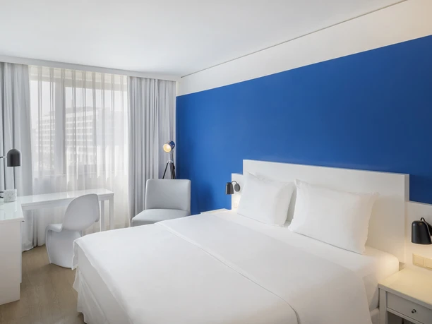 Frankfurt Messe Affiliated by Meliá-- Hotelzimmer Helles Hotelzimmer mit weißem Bett und blauer Wand.