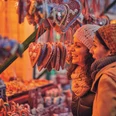 Otterndorfer Sternenmarkt Zwei Frauen betrachten lächelnd Lebkuchenherzen an einem festlich beleuchteten Weihnachtsmarktstand.