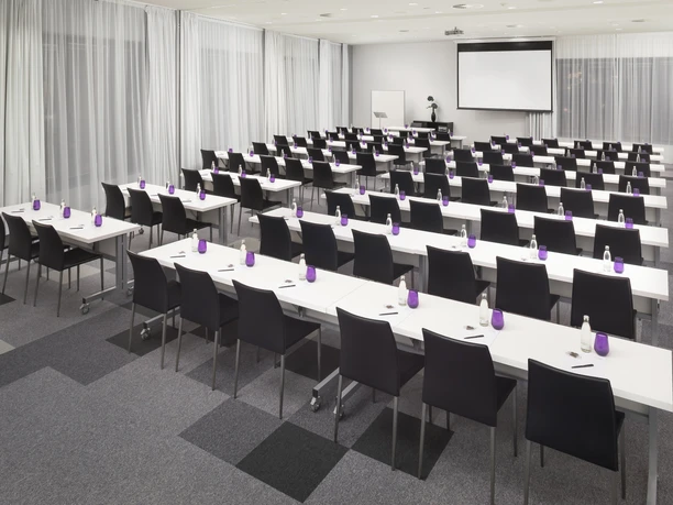INNSiDE Frankfurt Ostend - Tagungsraum Tagungsraum mit Tischreihen und Leinwand.