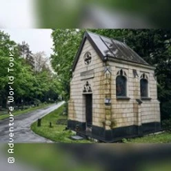 Kleines steinernes Mausoleum steht an einem kurvigen Weg zwischen hohen Bäumen.