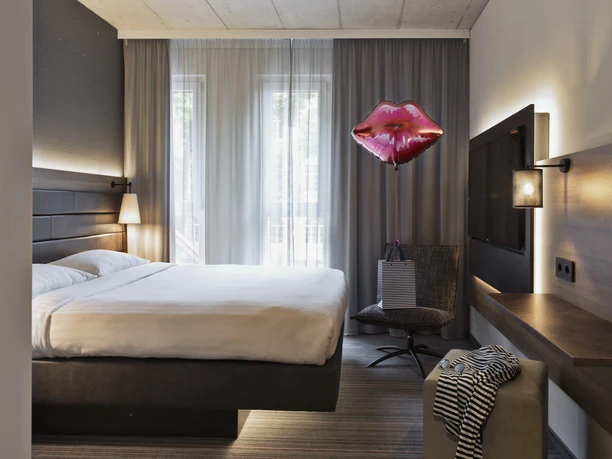 Moxy Frankfurt East - Hotel rooms Modern hotel room with bed and balloon.