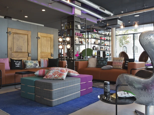 Moxy Frankfurt East - Lounge Bunte Lounge im Industrial-Design mit Ledersofas.