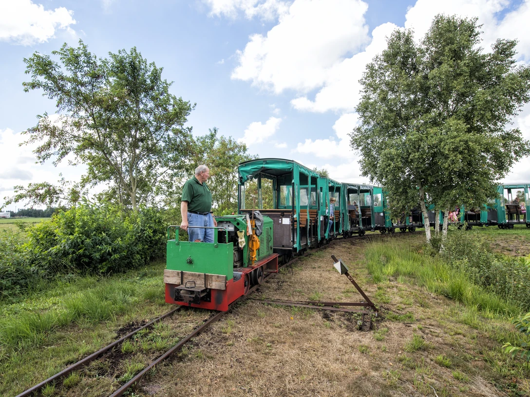 Moorbahn Ahlenmoor Grüne Moorbahn mit offenen Waggons fährt durch eine Moorlandschaft mit Wiesen, Bäumen und blauem Himmel.Green moor railroad with open wagons runs through a moor landscape with meadows, trees and blue sky.Den grønne hedejernbane med åbne vogne kører gennem et hedelandskab med enge, træer og blå himmel.De groene veenbaan met open wagons rijdt door een veenlandschap met weiden, bomen en blauwe lucht.