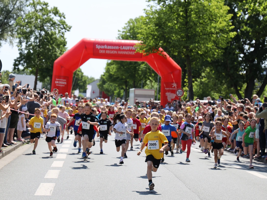 Stadtlauf_3626-os A 1366.jpg Kinder starten beim Stadtlauf unter rotem Torbogen, umgeben von jubelnden Zuschauerreihen.Children start the city run under a red archway, surrounded by rows of cheering spectators.Børnene starter byløbet under en rød buegang, omgivet af rækker af jublende tilskuere.Kinderen beginnen de stadsloop onder een rode boog, omringd door rijen juichende toeschouwers.