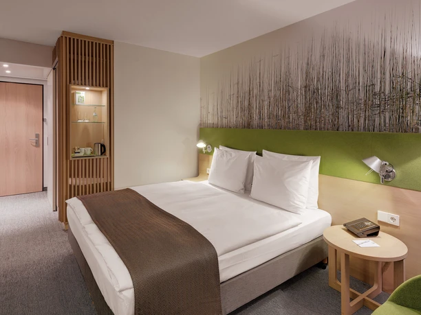 Holiday Inn Frankfurt - Alte Oper - Hotelzimmer Modernes Hotelzimmer mit Bett, Holz und grünen Akzenten.