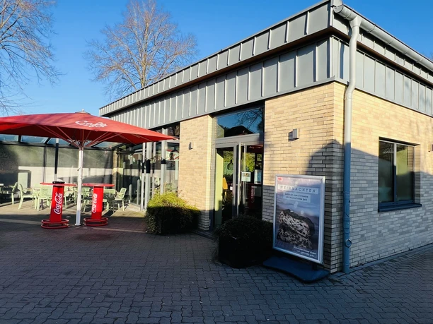 Modernes Gebäude mit heller Klinkerfassade, rotem Sonnenschirm und barrierefreiem Eingang.