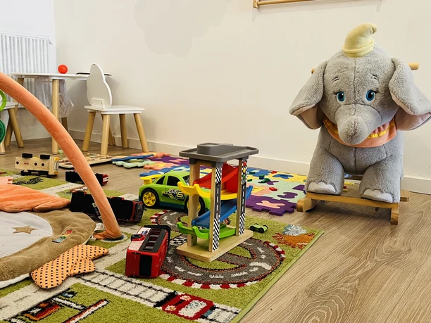 Spielecke im Café Heller Spielraum mit Teppich, Spielzeugautos, Holzrutsche und großem Plüschschaukelelefanten.