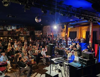 Music Hall Session Publikum lauscht einer Liveband in stimmungsvoll beleuchteter Music Hall mit Bühnenlicht und Technik.