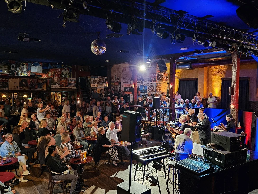 Music Hall Session Publikum lauscht einer Liveband in stimmungsvoll beleuchteter Music Hall mit Bühnenlicht und Technik.