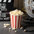 Kinoabend©Ali – stock.adobe.com_1303853794.jpg weiß-rot gestreifter Popcornbecher mit Popcorn gefüllt, steht vor einer alten Filmrolle