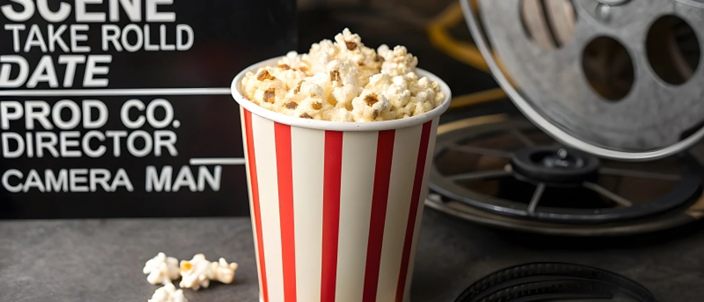 Kinoabend in Friedrichskoog weiß-rot gestreifter Popcornbecher mit Popcorn gefüllt, steht vor einer alten Filmrolle