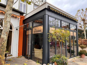 Eingang des Café Deutschmanek mit gläsernem Wintergarten und Herbstlaub vor der Fassade