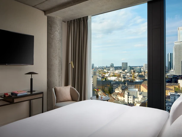 NH Collection Frankfurt Spin Tower - Hotelzimmer Hotelzimmer mit großem Bett und direktem Blick auf die Frankfurter Skyline durch die bodentiefen Fenster.
