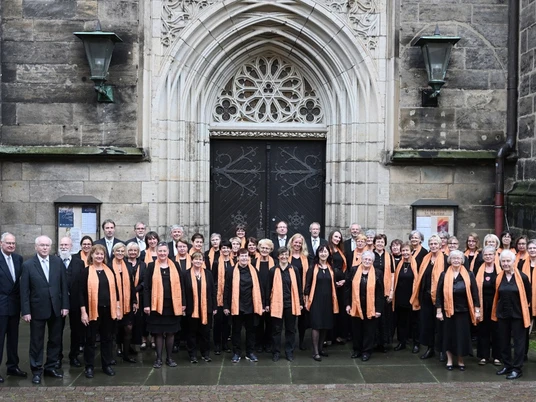 Pirna-Chor_030-1506-24_028Pirna-Chor_030-1506-24.JPG Eine Gruppe von Chormitgliedern steht vor einem prunkvollen, gotischen Kirchenportal.