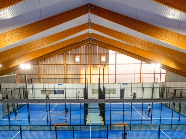 Padelhalle.jpg Mehrere Menschen spielen Padel in einer großen Halle mit blauem Boden.