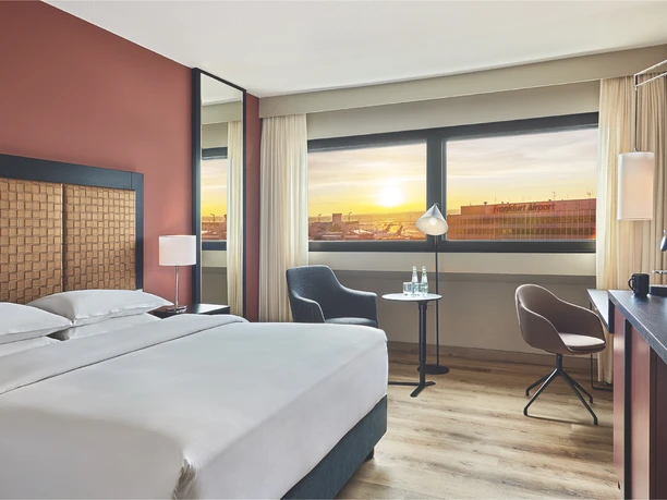 Marriott Sheraton Frankfurt Airport Hotels - Hotelzimmer Hotelzimmer mit großem Bett und Abendblick durch das Fenster auf das Flughafengelände.