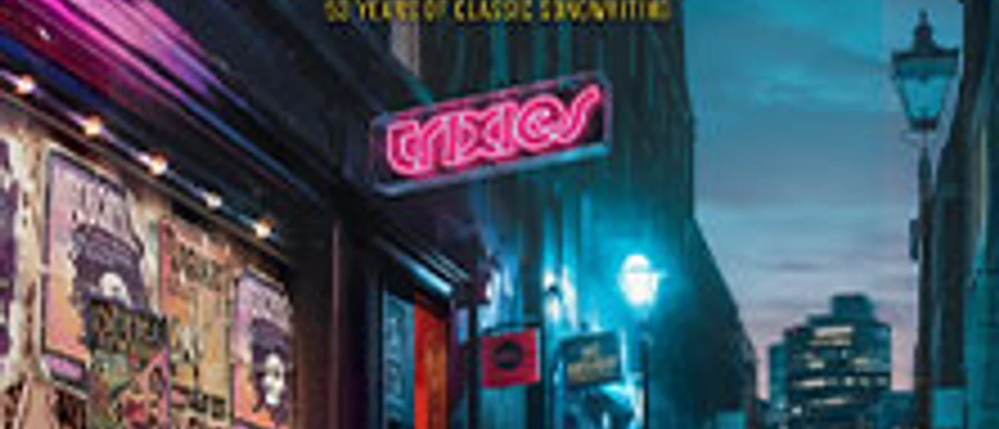 Bunt beleuchtete Straße in Köln bei Nacht mit Konzertplakaten an einer Backsteinwand.