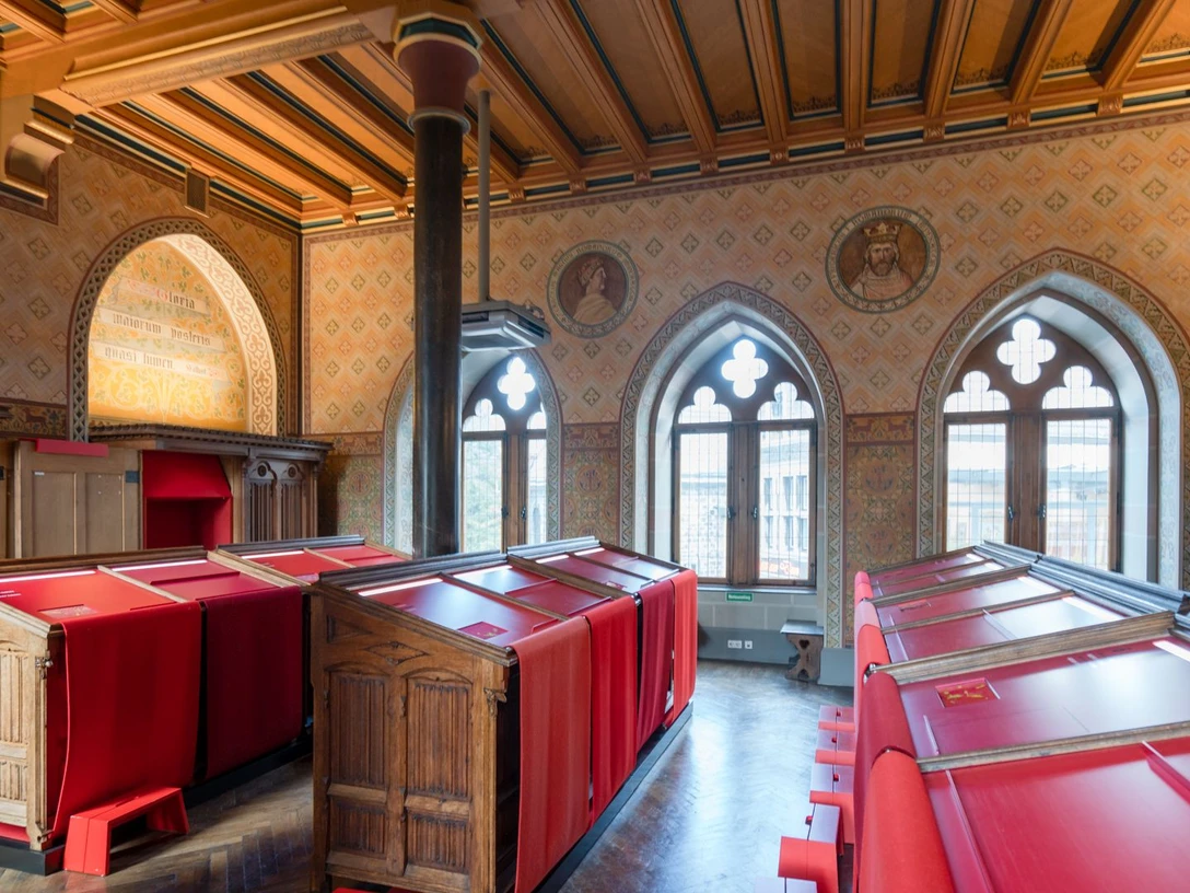 2022-08 Grashaus 3 (c) aachenviews.jpg Historischer Raum mit bogenförmigen Fenstern und hölzernen Tresen, die von roten Tüchern überzogen sind.