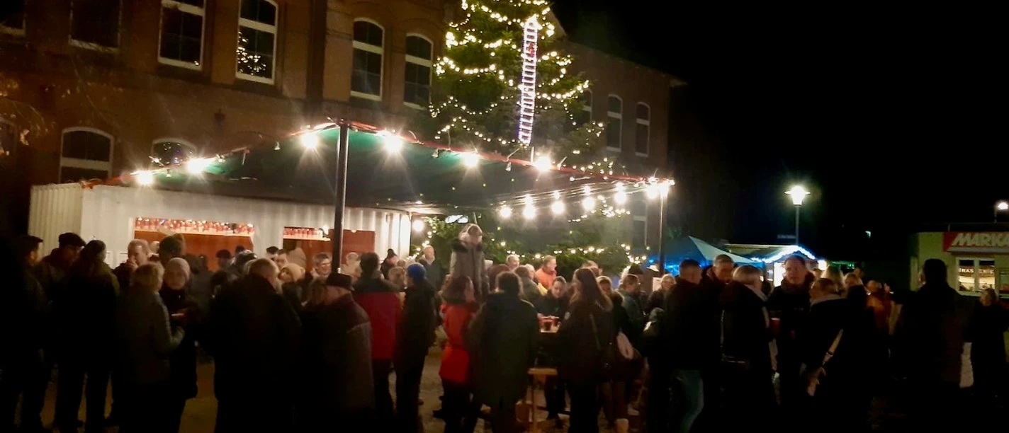 Glühweinabend beim OBV Apen.jpg Menschen stehen bei Nacht auf dem Rathausmarkt Apen, Lichterketten und Tannenbaum erhellen den Platz.