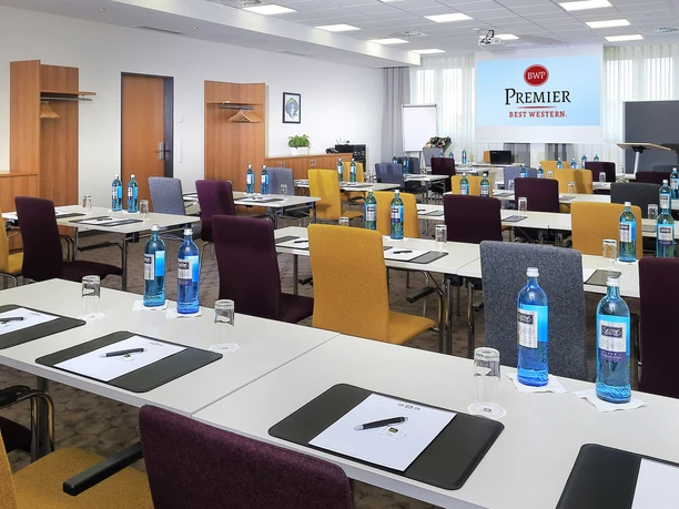 Best Western Premier IB Hotel Friedberger Warte - Adorno+Fromm Tagungsraum mit bunten Stühlen und Leinwand.