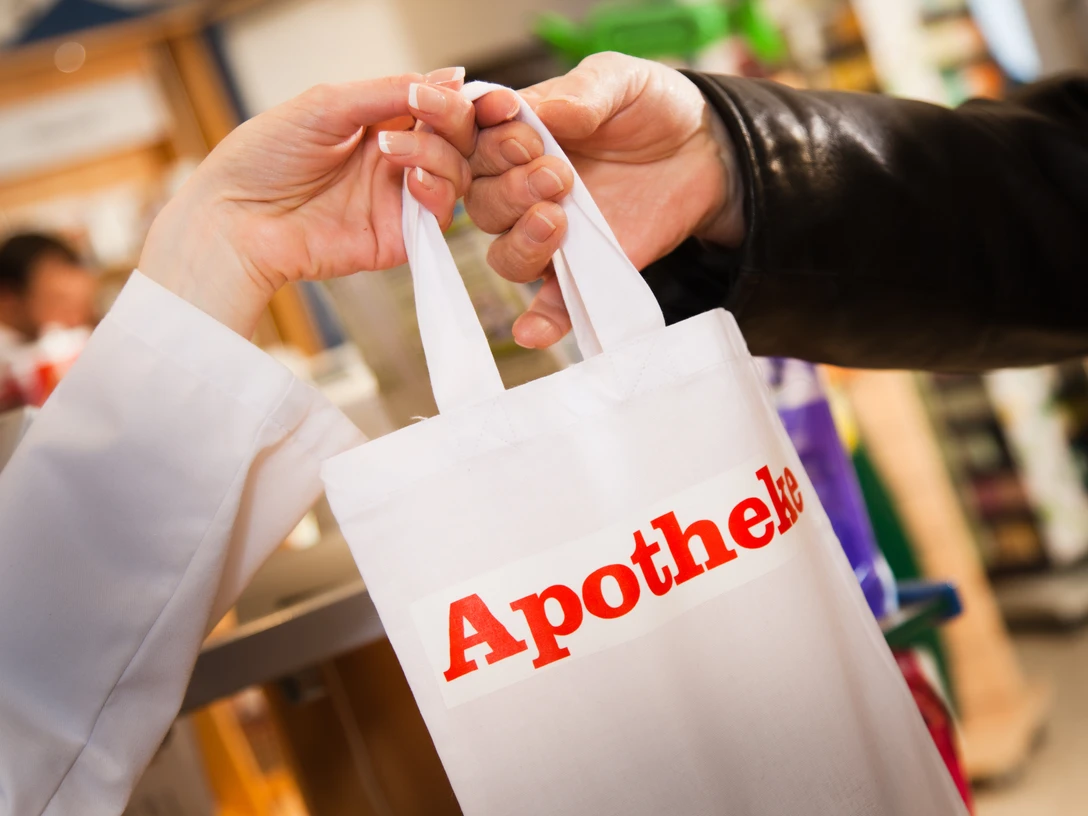 Die Apotheke Eine Person überreicht in einer Apotheke eine weiße Tüte mit roter Aufschrift „Apotheke“.