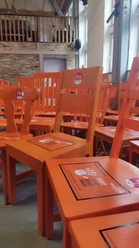 Reihe orangefarbener Stühle mit Plakaten gegen Gewalt an Frauen in einem Saal mit Holzbalken.