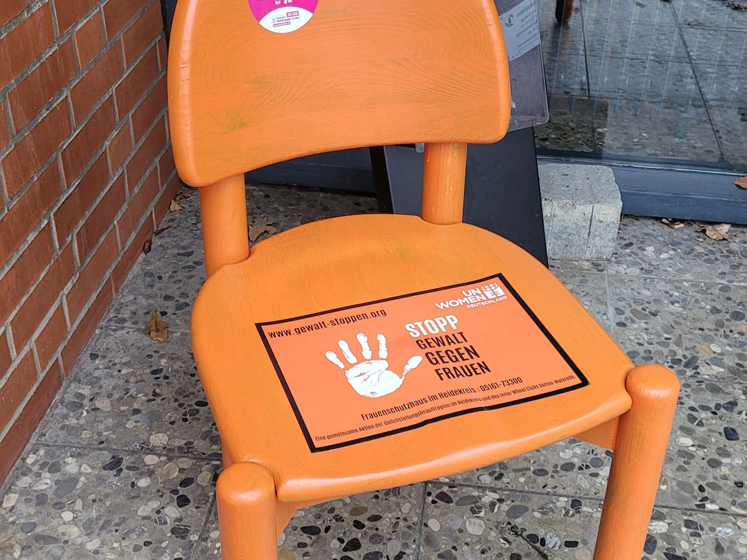 20251124_134156.jpg Oranger Stuhl mit Aufklebern gegen Gewalt an Frauen vor dem Rathaus Bispingen.