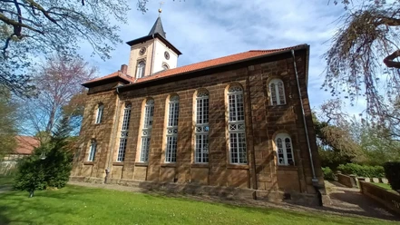 Christuskirche_Gitter (1)_HD_16zu9.jpg Historische Sandsteinkirche mit hohen Rundbogenfenstern, Turm mit Uhr und Spitzdach im Grünen.